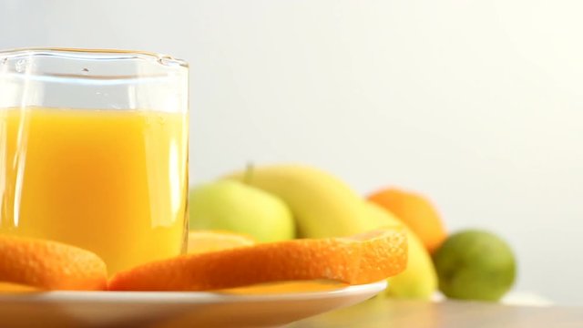 Fresh citrus fruits. Rotate Video footage of the concept of a healthy food and diet. Orange juice in a glass, with a background of different fruits: banana, lime, lemon, orange. It's spinning
