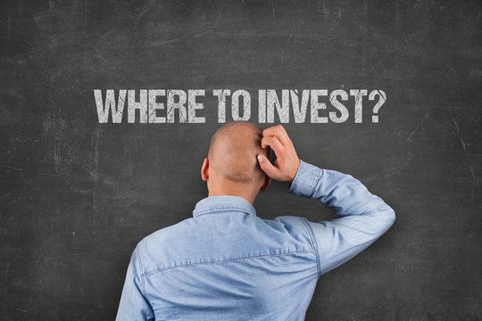 Confused Businessman Looking At Where To Invest Text On Blackboard
