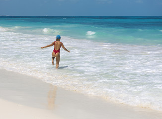 Sexy lady walking on the beach and splashing water happily. Turquoise water. Vacation concept image.