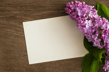 Pink lilac flowers with blank greeting card on the wooden table.