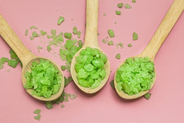 Green Salt in three wooden spoons on a pink background. Top view.
