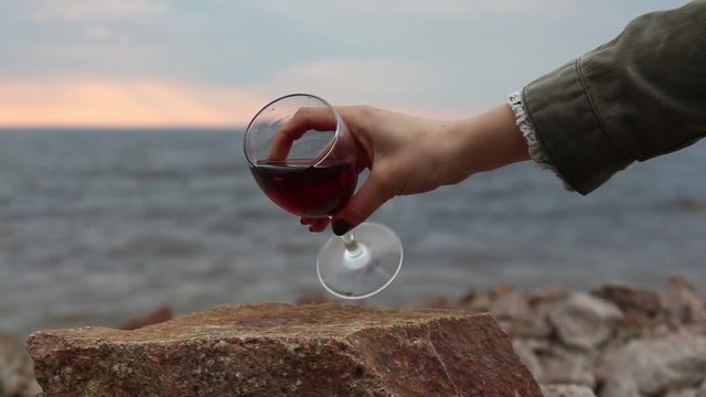 1080i. Girl pours red wine on a rocky beach near the sea. Slow motion