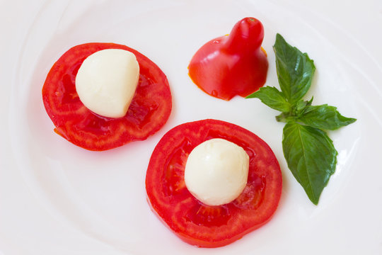 mozzarella on slices of tomato and green basil on white background