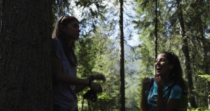 Woman playing joke scaring friend photographer in sunny forest woods. Group of friends summer adventure journey in mountain nature outdoors. Travel exploring Alps, Dolomites, Italy.4k slow motion 60p