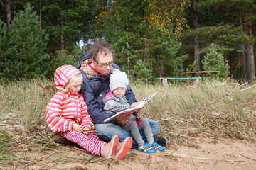 Fototapeta premium Father reads the book to his daughter in nature. Parental love.