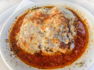 Aubergine, eggplant meal. Layers of aubergine with minced pork, and tomato. Cheese is melted and baked on the top. served in a white dish.