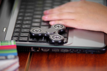 Young woman working in the computer and a popular fidget spinner toy over the laptop, on office...