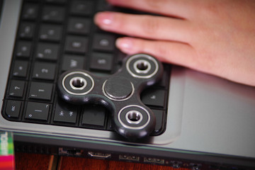 Young woman working in the computer and a popular fidget spinner toy over the laptop, on office background