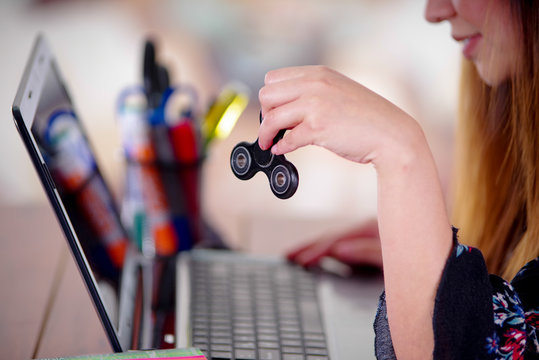 Young woman holding a popular fidget spinner toy in her hand while she is working in her computer on office background