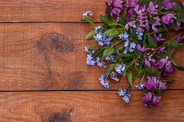 Fototapeta na wymiar brown wooden background with bunch of forget-me-nots, and dead-nettle