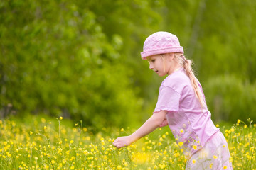 Adorable blonde girl in  pink hat and clothes posing on sunset on meadow with flowers
