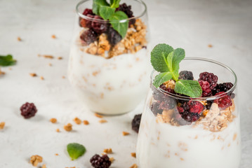 Dietary vegan healthy breakfast. Yogurt and granola with fresh blackberry oranges and mint in a glass. On a white table. Copy space close view