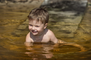 a little boy is sitting in the water and smiles on a summer day