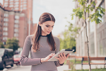 Young girl is studying in the spring park outside, browsing on her tablet, in casual comfortable outfit, focused and serious