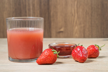 Ripe strawberry next to a glass of juice and strawberry jam on an old wooden table