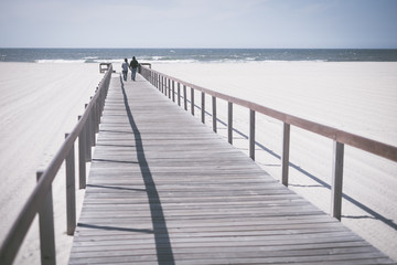 Obraz premium Para na spacerze chodnikiem do piaszczystej plaży w pobliżu morza, Kochający mężczyzna i kobieta podczas miesiąca miodowego nad morzem, Mężczyzna i kobieta na spacerze chodnikiem, Kochająca para w miesiącu miodowym, Romantyczny spacer po plaży nad morzem