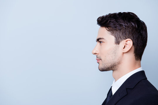 Side profile photo of a young handsome brunete realtor with bristle in a formal wear, standing on the pure blue background next to copyspace