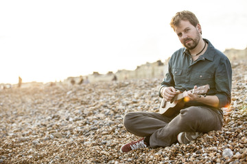 Young handsome man playing ukulele in an urban beach