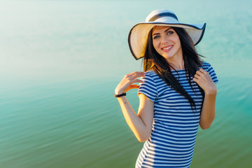 Woman in hat and striped dress on sea background smiling
