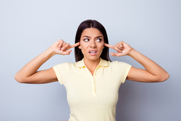 Close up of annnoyed young latinamerican girl, closing her ears with fingers. She is lookiing away  angry, she is in a casual tshirt on pure background