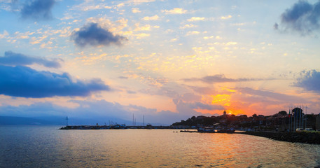 Sunrise on the Black Sea coast. Coastline of the old town Nesebar, Bulgaria. Sun rising on the background of the sky with cumulus clouds. Dawn at the seaside. Panoramic shot.