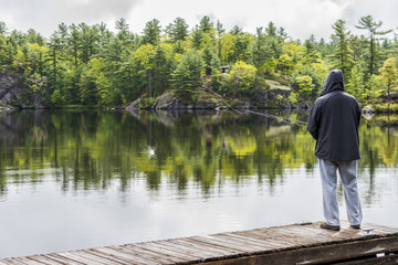 Man fishing off dock, line landing in water with small splash as he casts