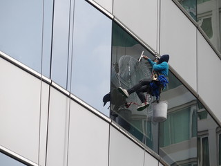 man cleaning glass building by rope access at height