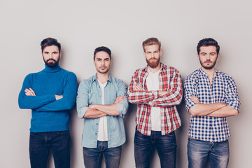 Ethnicity, multicultural diversity. Four serious harsh men are standing isolated on pure background with crossed hands, dressed in casual clothes and jeans