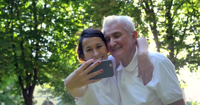 Granddaughter, a nurse, caring for the elderly, a girl (woman) and grandfather, do selfie, happy, smiles, in the park. Concept boarding house, sanatorium, house for the elderly, help for the elderly