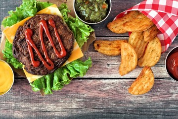 Picnic scene with barbecued hamburger and potato wedges over dark rustic wood