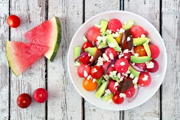Summer salad with watermelon, avocado, tomatoes and feta cheese, above scene on a rustic white wood...