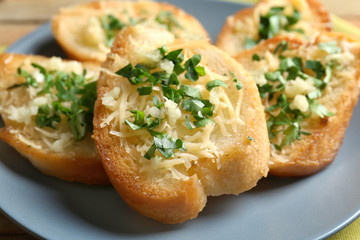 Tasty bread slices with grated cheese, garlic and herbs on plate