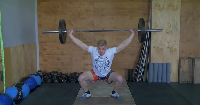 Muscular man doing the crossfit exercise in the gym. strong crossfit athlete in the middle a heavy snatch lift in a cross-fit box gym. One handsom man lifting barbel. Crossfit fitness gym