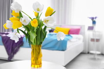 Vase with bouquet of white and yellow tulips in light room
