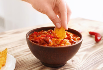 Female hand dipping nachos into bowl with chili turkey on wooden table, closeup