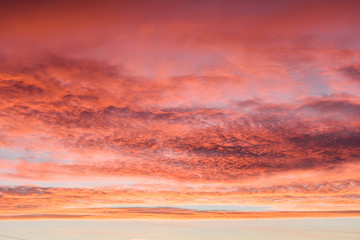 Beautiful fiery sunset sky with clouds painted in all shades of pink and orange