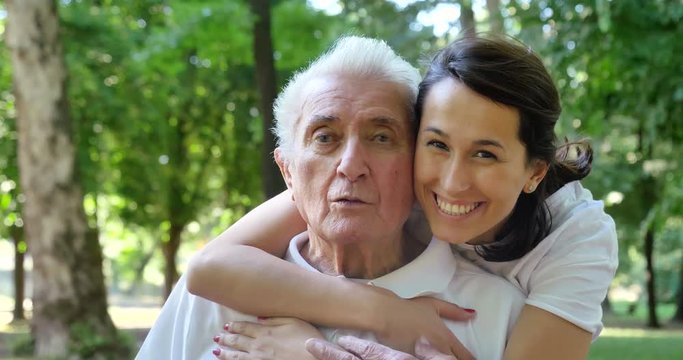 Granddaughter, nurse, caring for the elderly, girl (woman) hugging grandfather, smiling, happy, walking in the park. Concept: boarding house, sanatorium, a house for the elderly, help for the elderly.