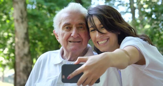 Granddaughter, a nurse, caring for the elderly, a girl (woman) and grandfather, do selfie, happy, smiles, in the park. Concept boarding house, sanatorium, house for the elderly, help for the elderly