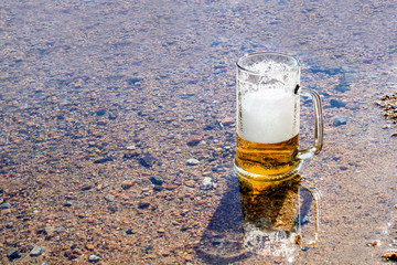 Mug of beer is cooled in a mountain river