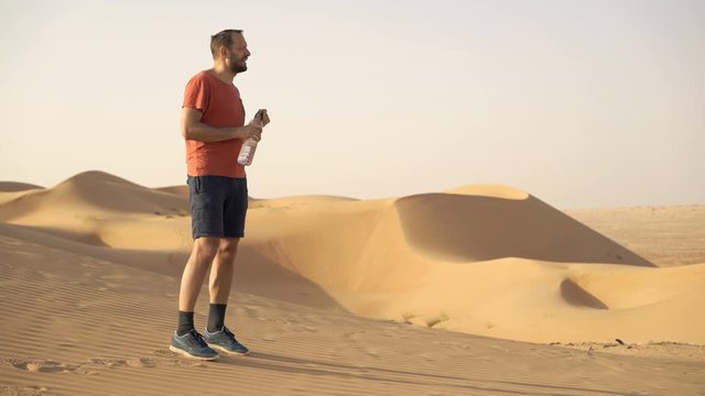 Young man drinking water and walking on desert
