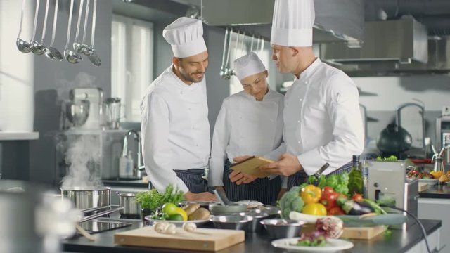 In the Modern Kitchen Team of Cooks Use Tablet Computer For Recipes, They Smile and Have Discussion. Shot on RED EPIC-W 8K Helium Cinema Camera.