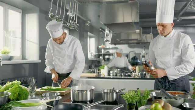 Two Famous Chefs Work as a Team in a Big Restaurant Kitchen. Vegetables and Ingredients are Everywhrere, Kitchen Looks Modern with Lots of Stainless Steel.Shot on RED EPIC-W 8K Helium Cinema Camera.