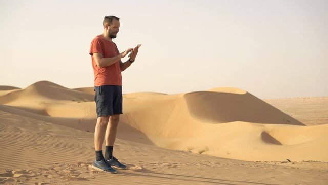 Young man with tablet checking map and walking on dessert
