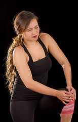 Beautiful young attractive sport woman holding injured knee suffering pain, in black background