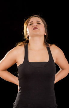 Young beautiful sportwoman suffer cervical pain in her lower back, in black background