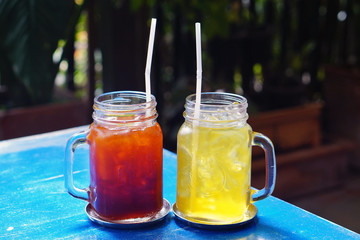 Glass jars of Iced tea with lemon (Thai black tea) and Iced chrysanthemum tea on blue table.