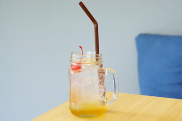 Closeup glass of Iced Passion fruit lemon soda topped with one red cherry on wooden table background, Summer Cocktail or Tropical Mocktail.