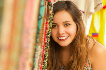 Close up of a beautiful smiling young woman hiding behind the andean traditional clothing textile yarn and woven by hand in wool, colorful fabrics background