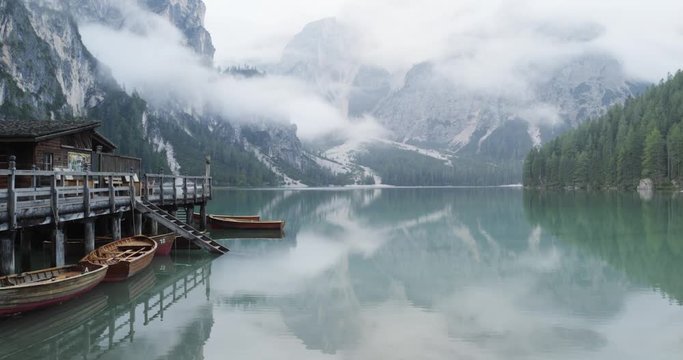 Small boathouse with wood pier and boats on Braies lake with cloudy weather.summer adventure journey in mountain nature outdoors. Travel exploring Alps, Dolomites, Italy. 4k slow motion 60p video