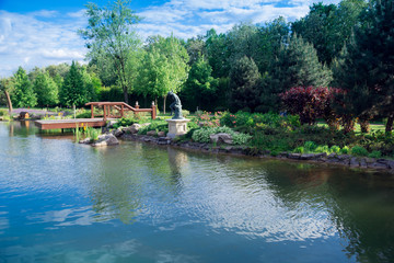 Obraz premium A lake in the middle of a green garden with bridge, statue and forest